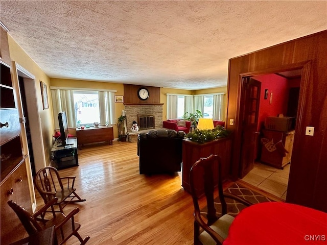 living room featuring hardwood / wood-style floors, a stone fireplace, a wealth of natural light, and a textured ceiling