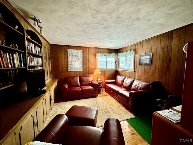 living room with wooden walls, a textured ceiling, and light wood-type flooring