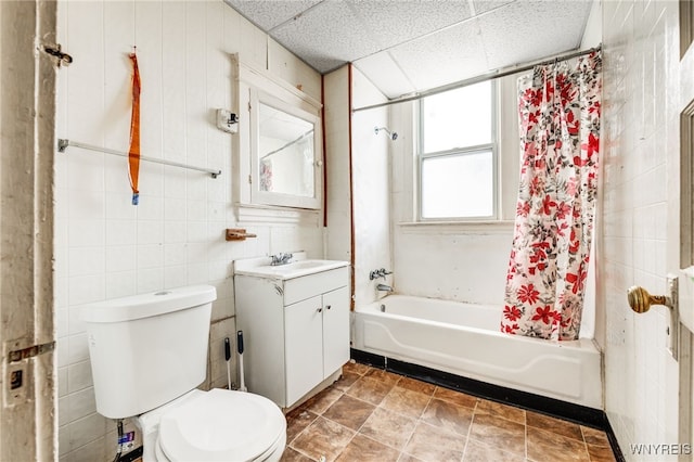 full bathroom with a paneled ceiling, tile walls, vanity, toilet, and shower / bath combo with shower curtain