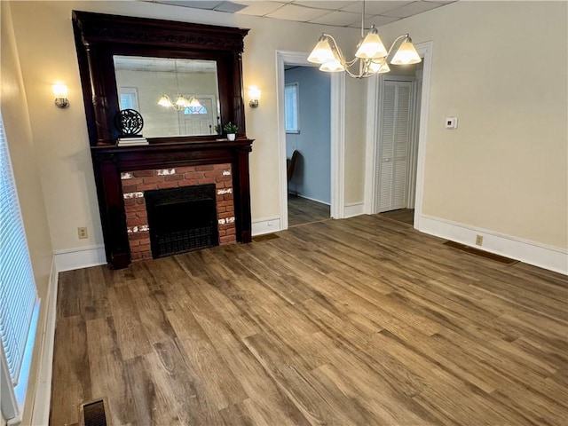 unfurnished living room featuring a brick fireplace, hardwood / wood-style floors, and a chandelier