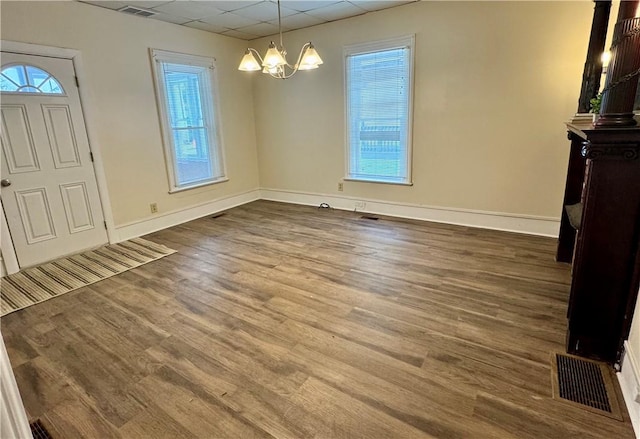 unfurnished dining area featuring an inviting chandelier, a paneled ceiling, wood-type flooring, and plenty of natural light