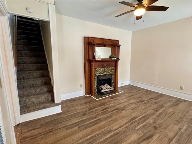 unfurnished living room featuring a tile fireplace, dark hardwood / wood-style floors, and ceiling fan