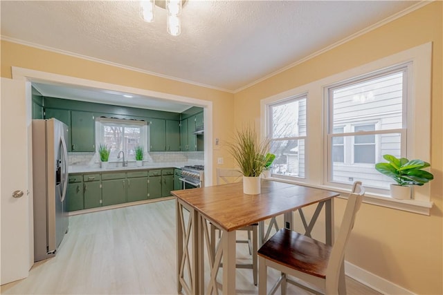 dining space with a healthy amount of sunlight, sink, crown molding, and light hardwood / wood-style flooring