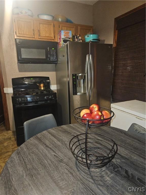 kitchen featuring dark tile patterned floors, light brown cabinetry, and black appliances