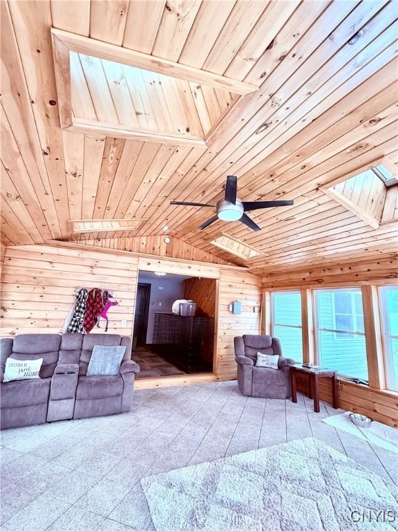 tiled living room featuring ceiling fan, vaulted ceiling with skylight, wood ceiling, and wood walls