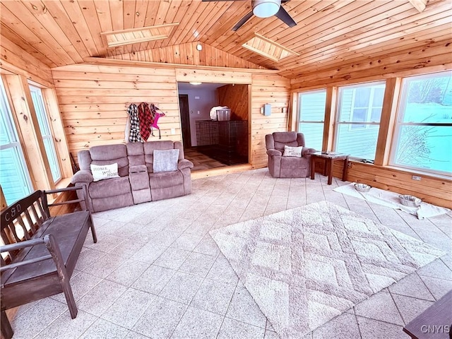 living room featuring ceiling fan, wooden ceiling, vaulted ceiling with skylight, and wood walls