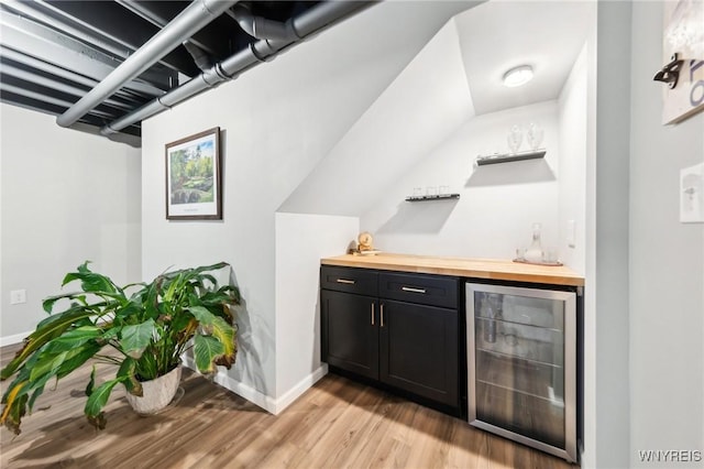 bar featuring beverage cooler, butcher block countertops, and light hardwood / wood-style flooring