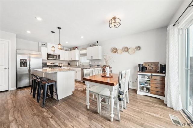 kitchen with a kitchen island, appliances with stainless steel finishes, white cabinets, hanging light fixtures, and light hardwood / wood-style floors