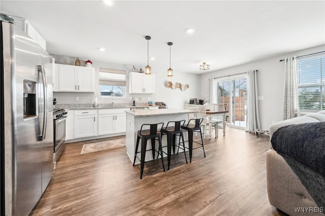 kitchen with appliances with stainless steel finishes, a kitchen breakfast bar, a kitchen island, pendant lighting, and white cabinets