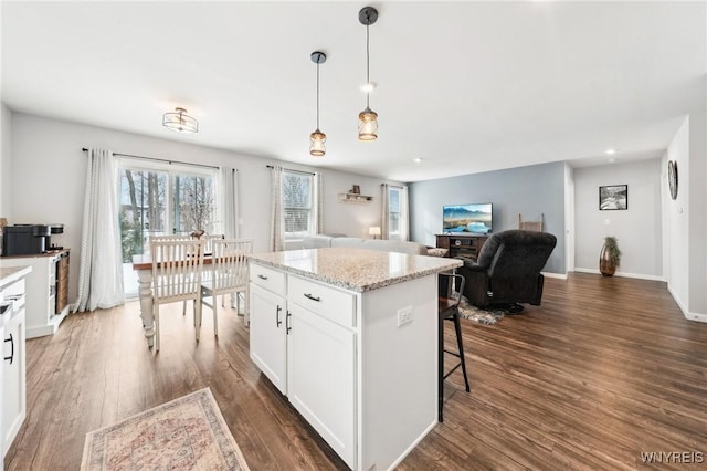 kitchen with a kitchen island, dark hardwood / wood-style floors, pendant lighting, white cabinets, and light stone counters