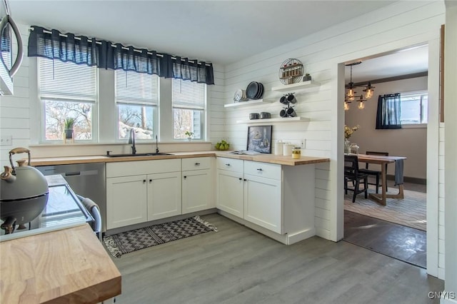 kitchen featuring wood counters, sink, wood walls, white cabinetry, and light hardwood / wood-style floors