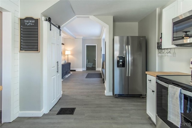 kitchen with butcher block countertops, white cabinetry, stainless steel appliances, a barn door, and light hardwood / wood-style flooring