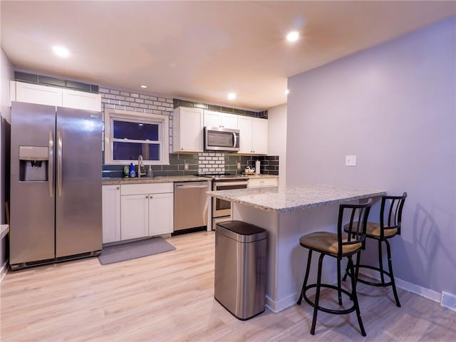 kitchen featuring backsplash, stainless steel appliances, light stone countertops, and white cabinets