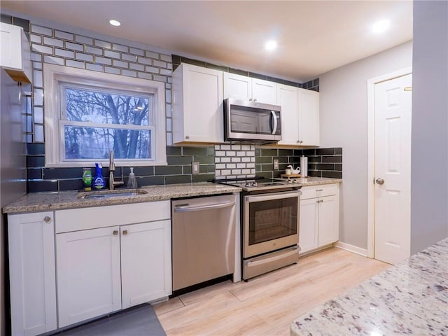 kitchen featuring tasteful backsplash, white cabinetry, sink, stainless steel appliances, and light stone countertops