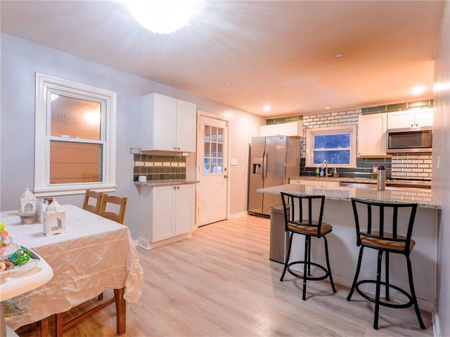 kitchen with white cabinetry, stainless steel appliances, a kitchen breakfast bar, and light stone countertops