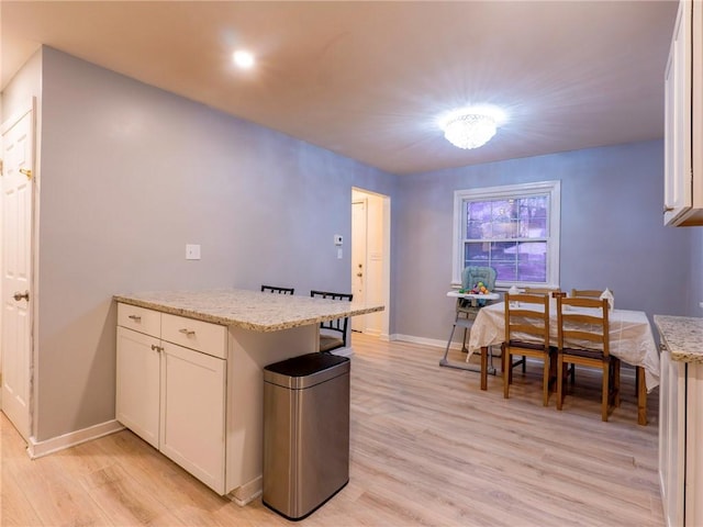 kitchen with white cabinetry, light stone counters, and light wood-type flooring