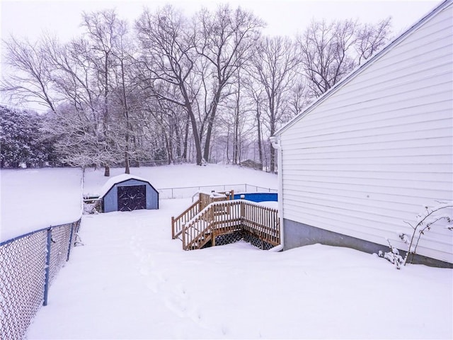 yard covered in snow featuring a wooden deck and a storage shed