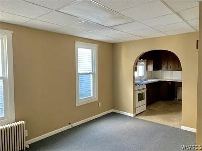 kitchen with carpet floors, white range, radiator heating unit, and a drop ceiling