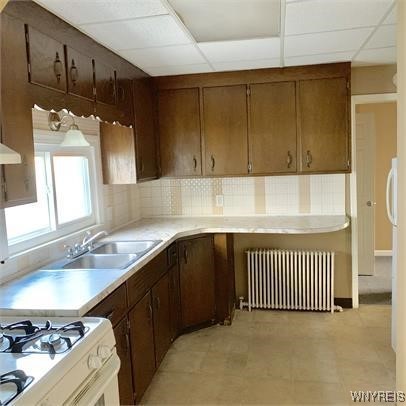 kitchen featuring a drop ceiling, backsplash, radiator heating unit, and sink