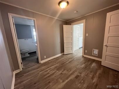 unfurnished bedroom featuring crown molding and dark wood-type flooring