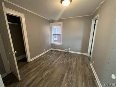 unfurnished bedroom featuring crown molding, dark wood-type flooring, and a closet