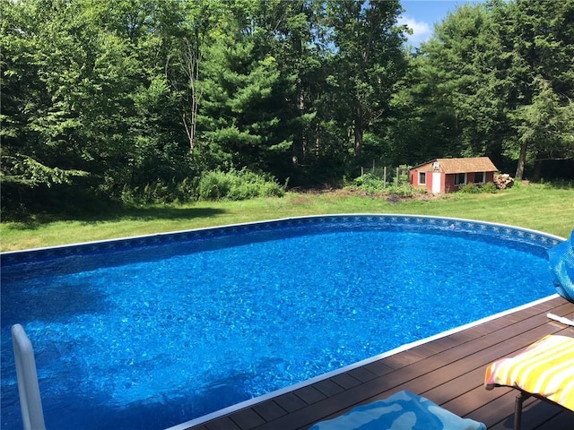 outdoor pool with an outdoor structure, a wooden deck, and a yard