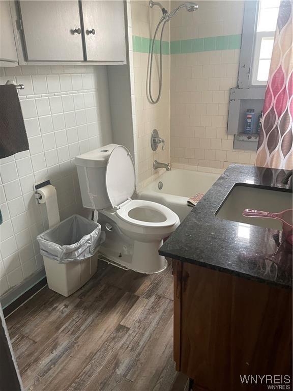 full bathroom with toilet, wood-type flooring, tile walls, vanity, and tiled shower / bath combo