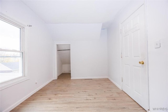 unfurnished bedroom with a walk in closet, lofted ceiling, and light hardwood / wood-style flooring