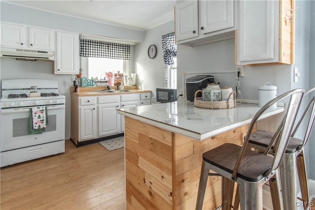 kitchen with a kitchen bar, sink, white range with gas stovetop, white cabinetry, and light wood-type flooring