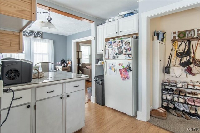 kitchen with white refrigerator, white cabinetry, hanging light fixtures, and light wood-type flooring