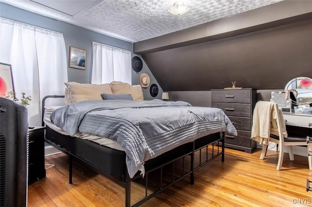 bedroom featuring vaulted ceiling, light hardwood / wood-style flooring, and a textured ceiling