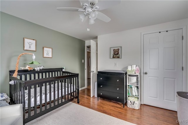 bedroom with ceiling fan, hardwood / wood-style floors, and a crib