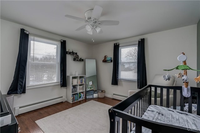 bedroom featuring baseboard heating, ceiling fan, a nursery area, and dark hardwood / wood-style flooring