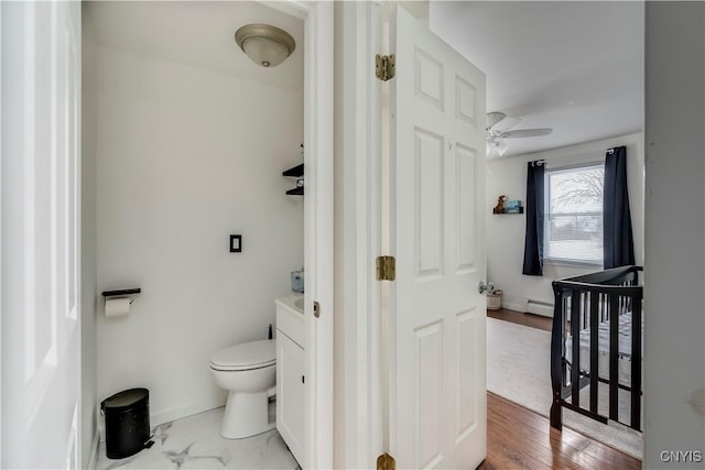 bathroom with hardwood / wood-style flooring, ceiling fan, a baseboard heating unit, vanity, and toilet