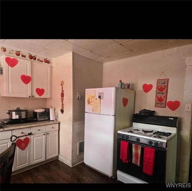 kitchen featuring dark wood-type flooring, a drop ceiling, white cabinets, and white appliances