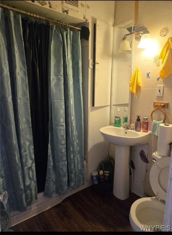 bathroom with a shower with curtain, toilet, hardwood / wood-style floors, and tile walls