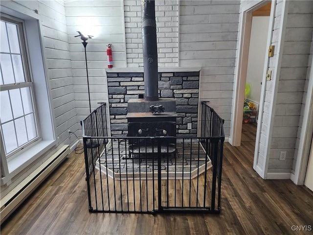 interior details featuring a baseboard heating unit, wooden walls, hardwood / wood-style floors, and a wood stove