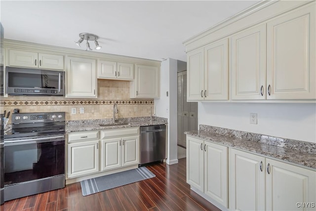 kitchen featuring sink, dark wood-type flooring, stainless steel appliances, tasteful backsplash, and light stone counters