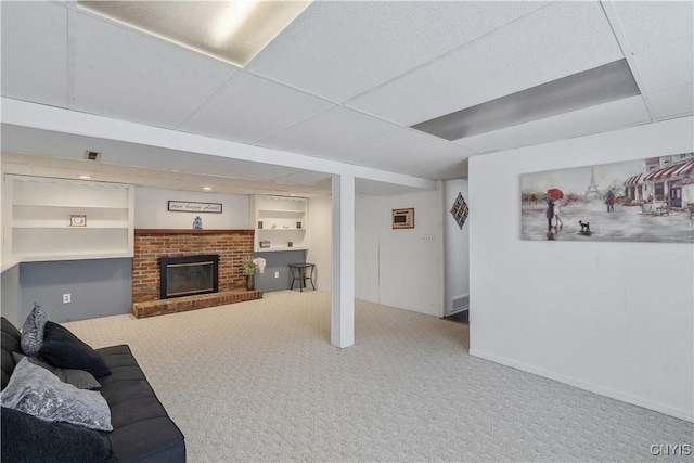 living room with built in shelves, a fireplace, carpet, and a drop ceiling