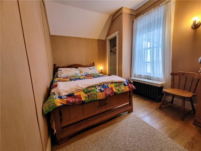 bedroom featuring vaulted ceiling, radiator, wooden walls, and light hardwood / wood-style floors