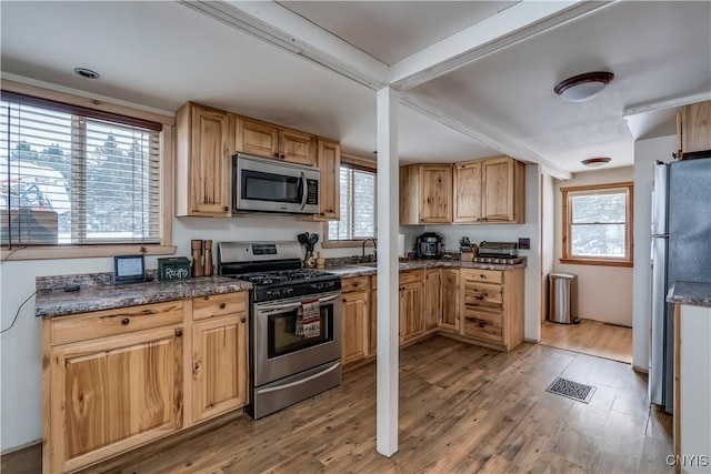 kitchen with a healthy amount of sunlight, stainless steel appliances, light hardwood / wood-style floors, and dark stone counters