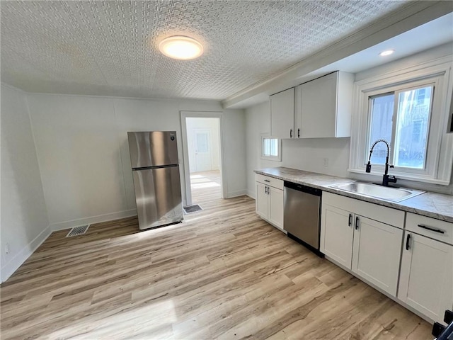 kitchen with sink, appliances with stainless steel finishes, white cabinetry, light hardwood / wood-style floors, and a textured ceiling