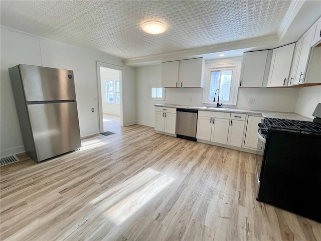 kitchen with appliances with stainless steel finishes, sink, white cabinets, and light hardwood / wood-style flooring