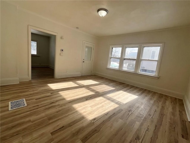 spare room featuring ornamental molding, plenty of natural light, and light hardwood / wood-style flooring