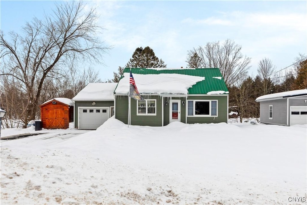 view of front facade with an outbuilding, metal roof, a storage shed, and an attached garage