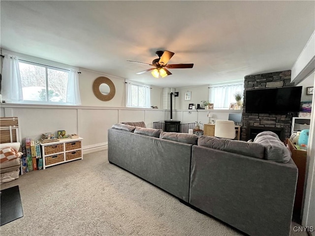 living room featuring a stone fireplace, ceiling fan, and carpet flooring