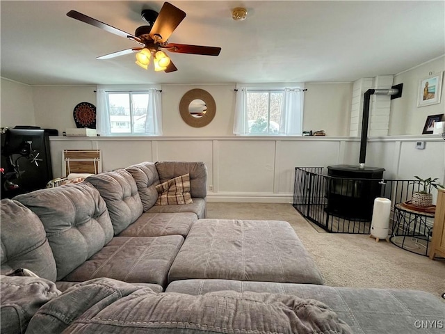 living room featuring light carpet, a wealth of natural light, ceiling fan, and a wood stove