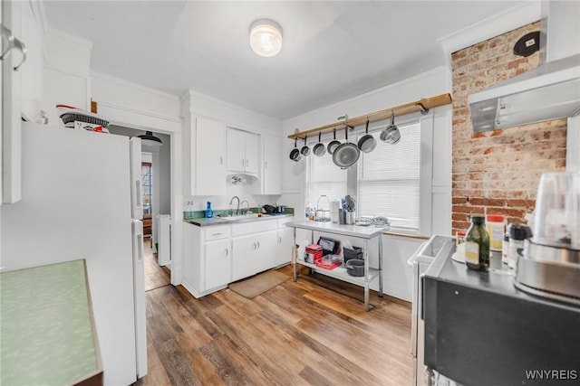 kitchen featuring sink, white cabinetry, light wood-type flooring, white refrigerator, and brick wall