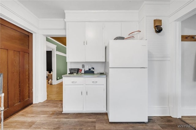 kitchen with white refrigerator, ornamental molding, light wood-type flooring, and white cabinets