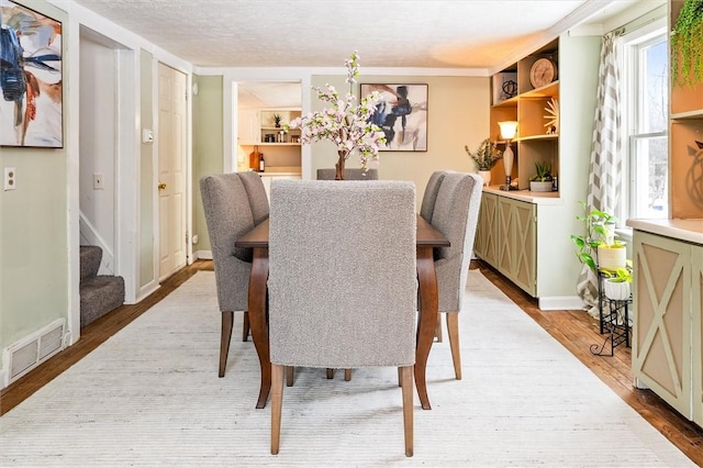 dining room with built in features, light hardwood / wood-style floors, and a textured ceiling